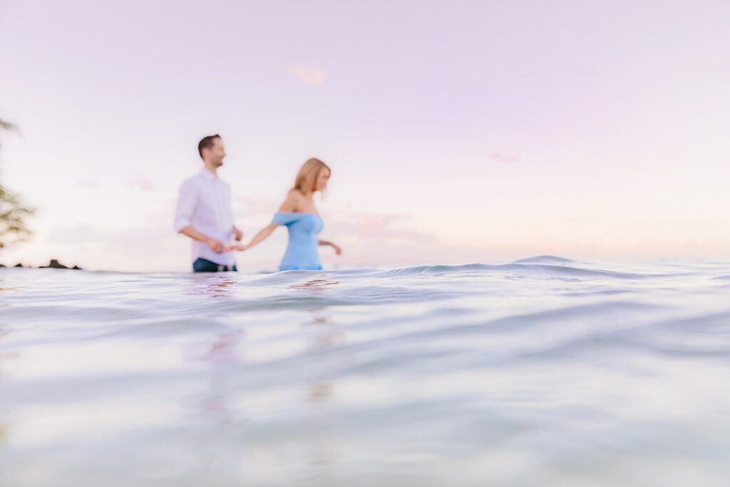 intentionally blurry image of woman and man walking in to the hawaii ocean with the water in focus and couple out of focus