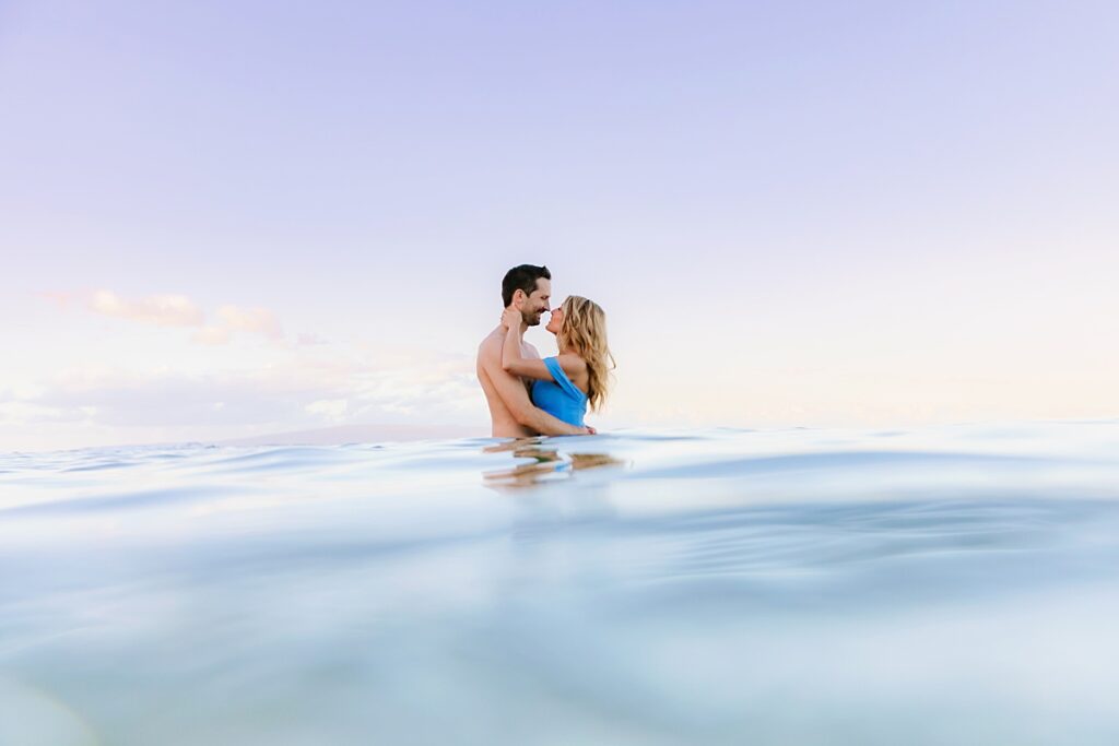 girl in blue dress wraps her arms around her husband in the ocean on maui