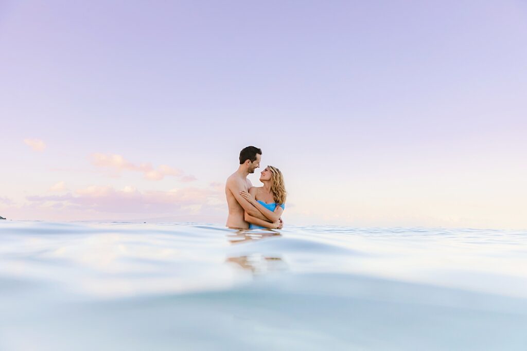 man and woman are in love and embrace in the sea wearing photoshoot attire