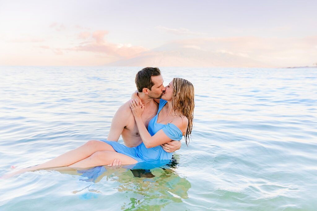 man lifts his wife out of the ocean and kisses her at sunrise on maui