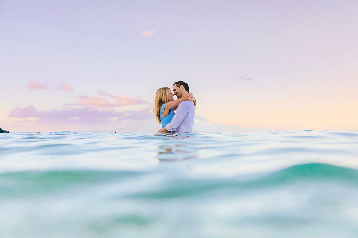 couple kisses in the ocean under beautiful pastel pink skies on maui during their honeymoon portrait shoot with love and water