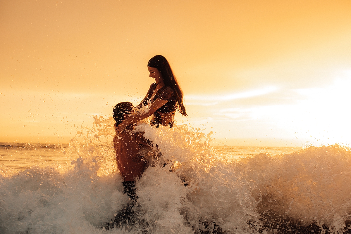 fun portrait of a couple splashing in the ocean at sunset with love and water