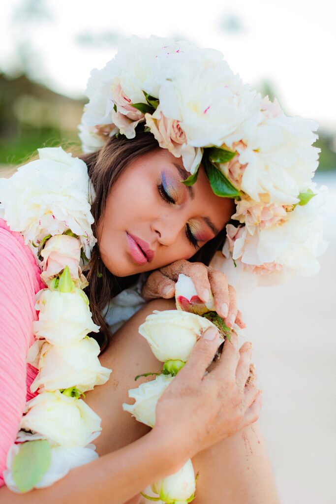 Close-up of the lei po’o worn by a woman photographed by love and water on Maui with soft flowers and greenery set against the pink fabric of her gown during her Wailea sunrise portraits.