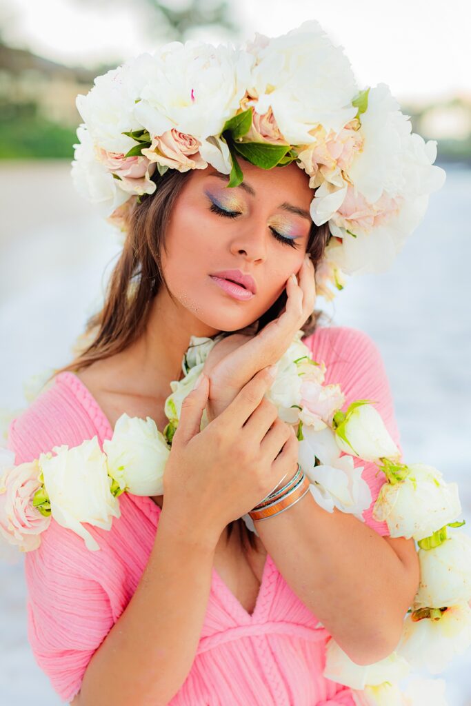 Close-up of the woman’s hands delicately holding her floral lei, with her shimmering mermaid-inspired makeup visible in the soft morning light.