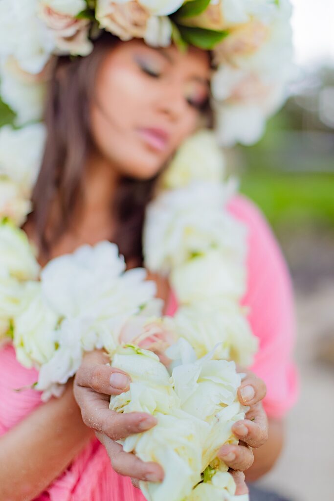 closeup of floral lei held by model wearing a pink gown on the beach in maui