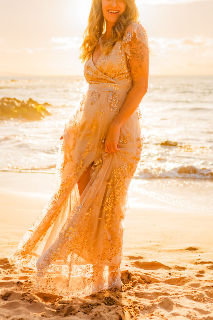 Backlit image of pregnant woman posing on Maui with love and water, wearing Baltic Born Corinne Shimmer Maxi gown at sunset