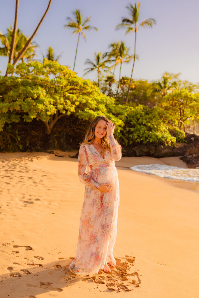 24 weeks pregnant woman in a flowing Baltic Born Layla tulle maxi dress standing on a Maui beach at sunset, captured by Love and Water Photography.