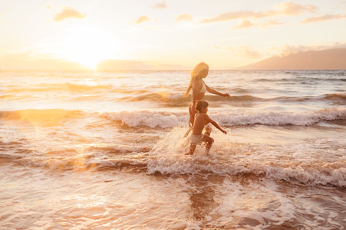 mom and son skip along the shoreline at the beach on maui during their love and water photoshoot