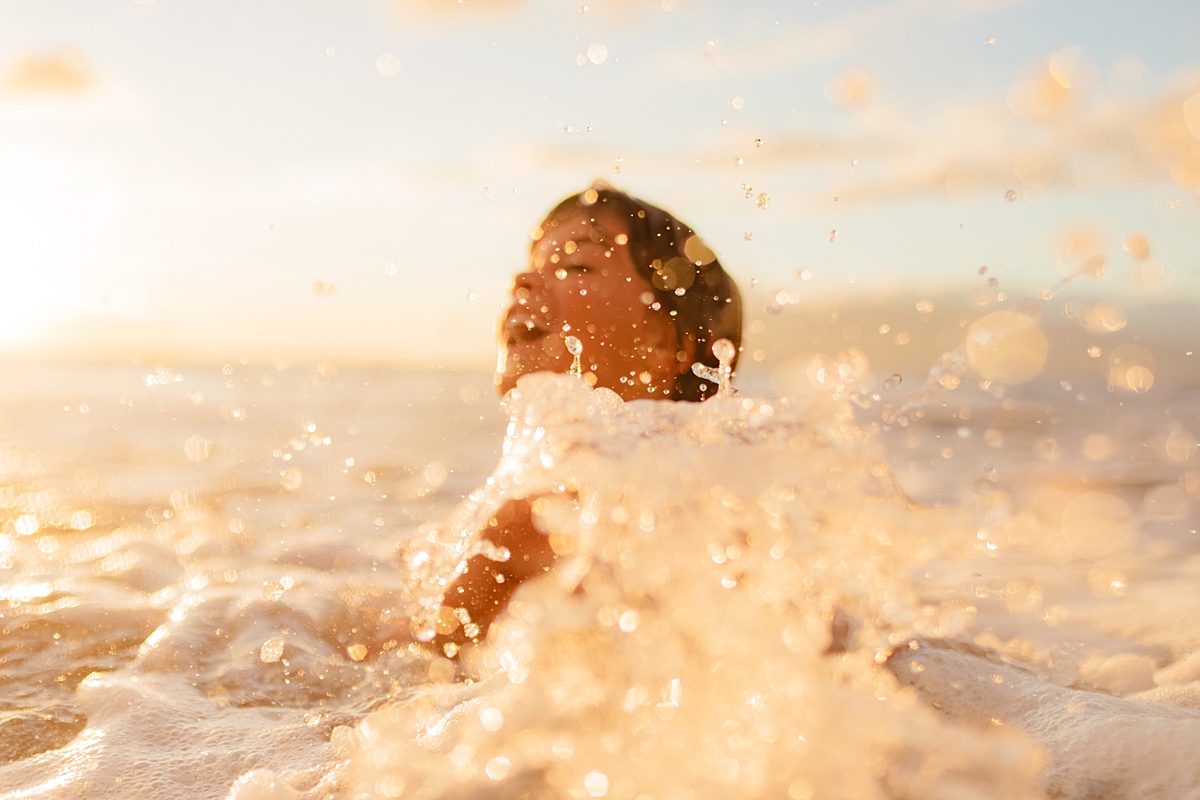 boy splashes with water bokeh at sunset in wailea photographed by love and water