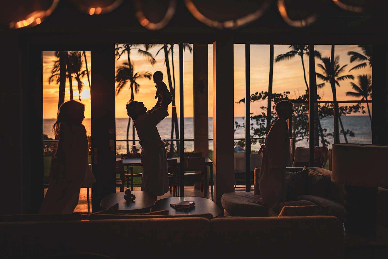 Young family silhouetted against the sunset in a large window looking out toward the ocean at Mokapu Beach from the makai oceanfront villa at andaz wailea