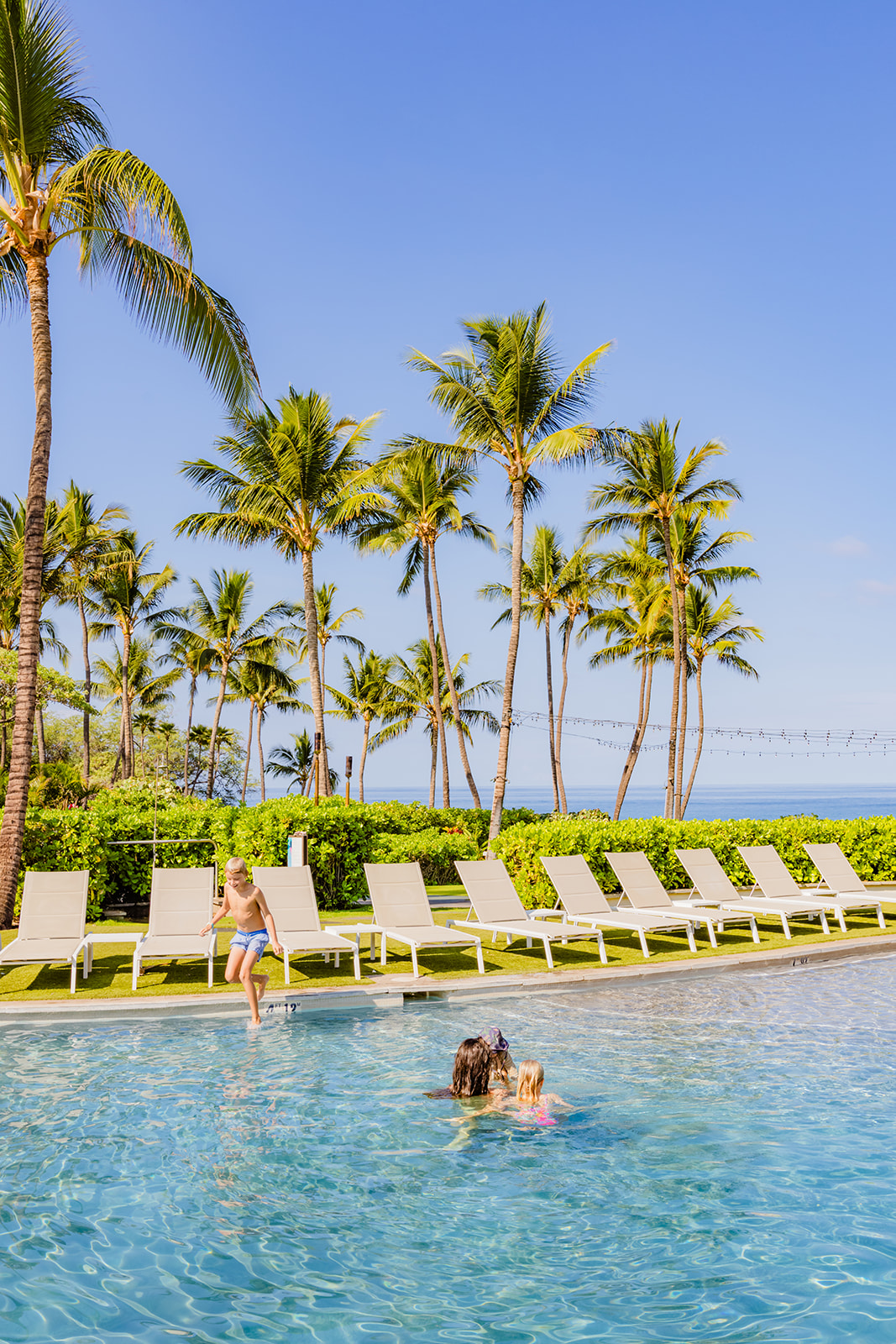 family enjoys the lower pool at andaz on a bright cloudless morning framed by green palmtrees